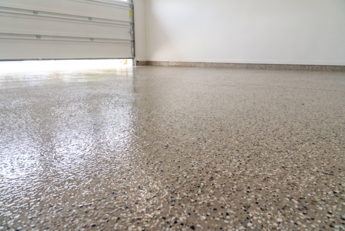 Illustration of a residential garage floor with a glossy tan and gray decorative flake epoxy coating beside a garage door